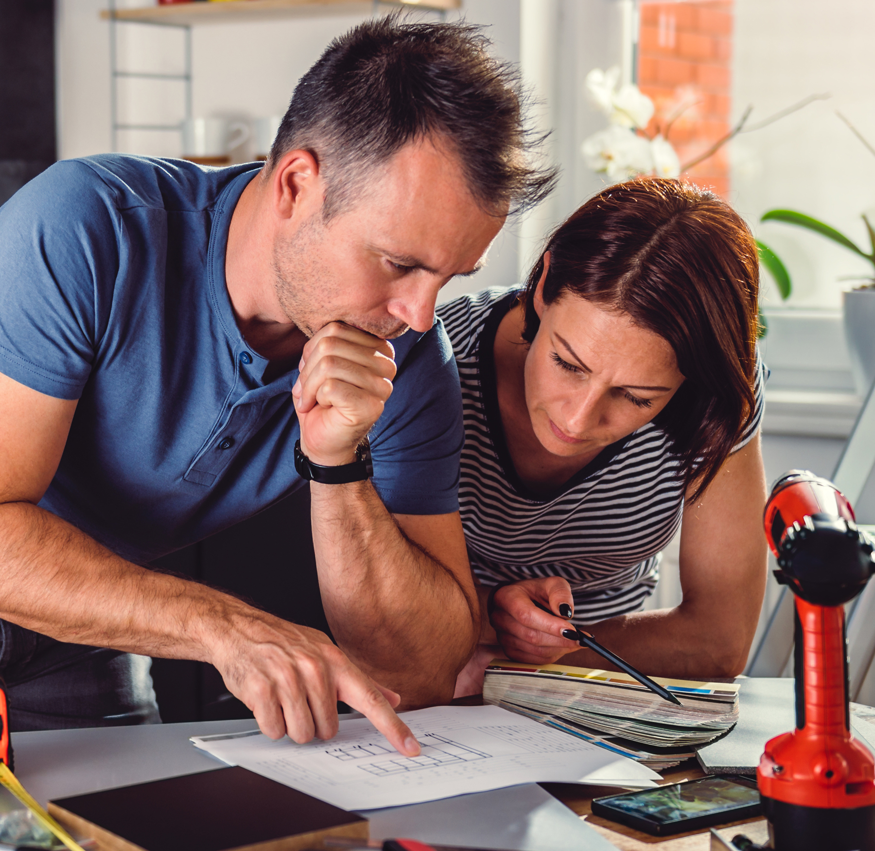 Man and women looking at home remodel plans with tools all around them. 